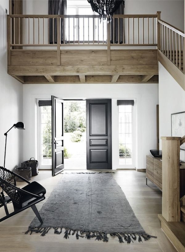 entrance with black double doors and gray rug paired with natural wood finishes ...