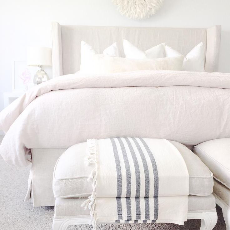 Monochromatic bedroom features a linen slipcovered wingback bed dressed in linen...