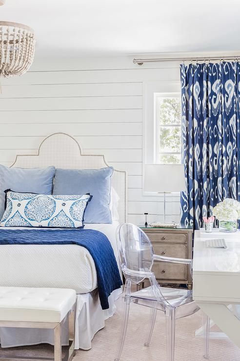 White and blue bedroom boasts shiplap walls lined with a white grid nailhead hea...