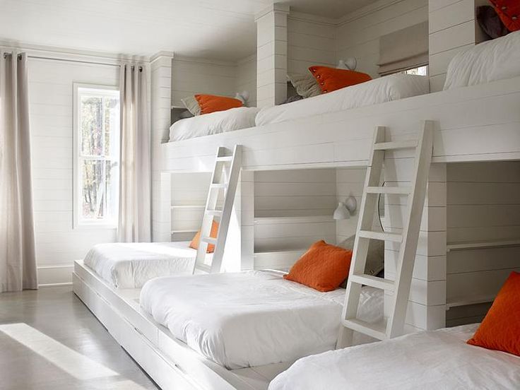 Country bunk room features a shiplap walls lined with a wall of three side by si...