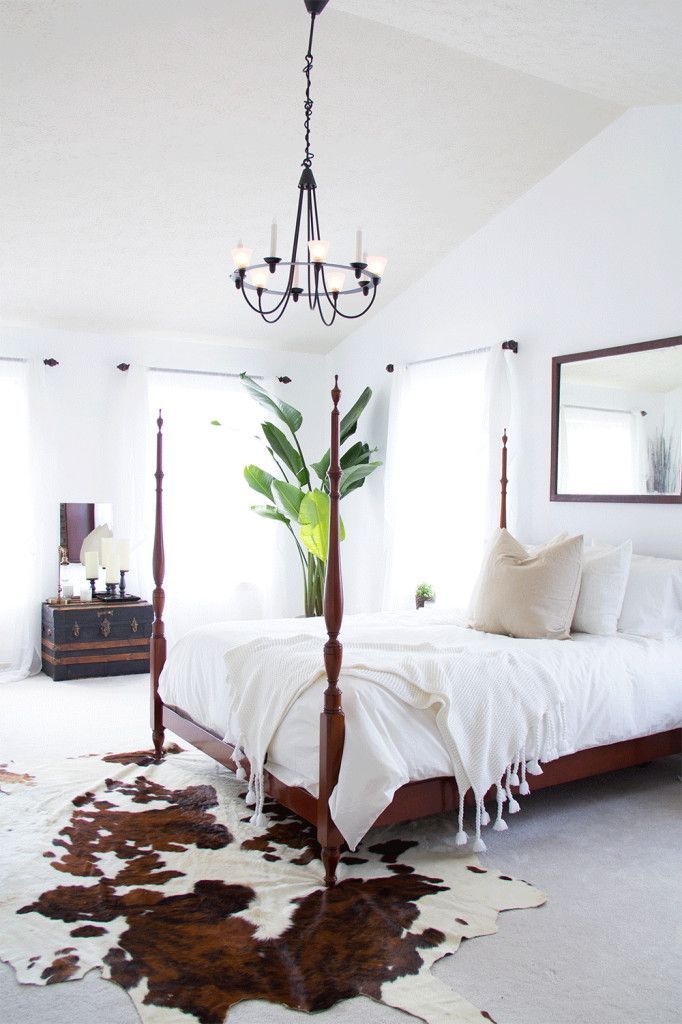 four poster bed with metal chandelier, and cowhide rug. simple and rustic bedroo...