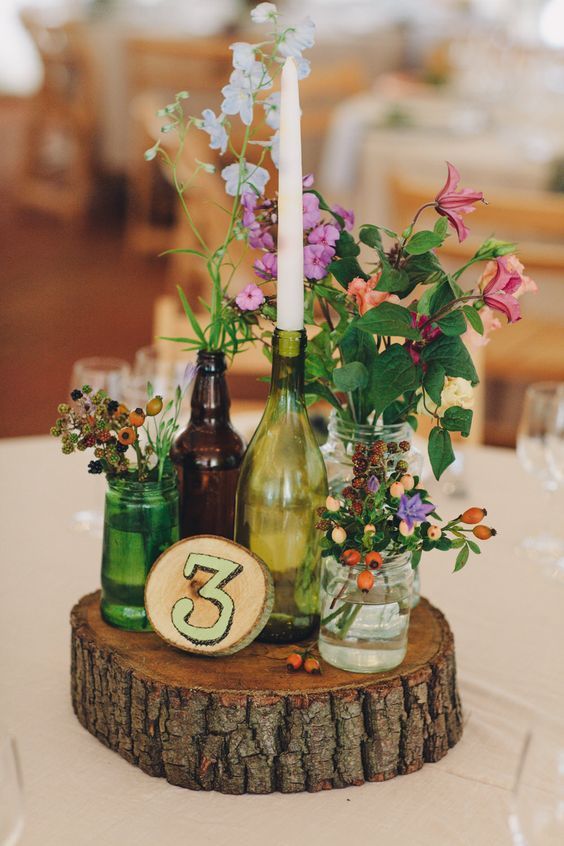Brown and green bottles on slabs of wooden tree stumps as table centre pieces wi...